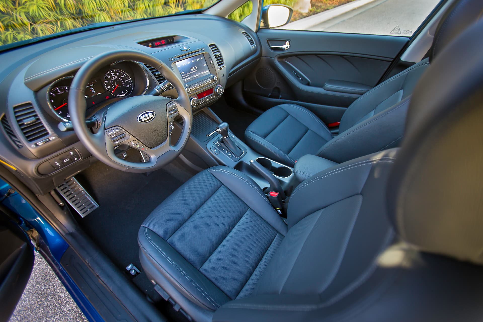 Kia Forte interior seen from above the driver's door, showing the steering wheel, center stack, console, and front seats