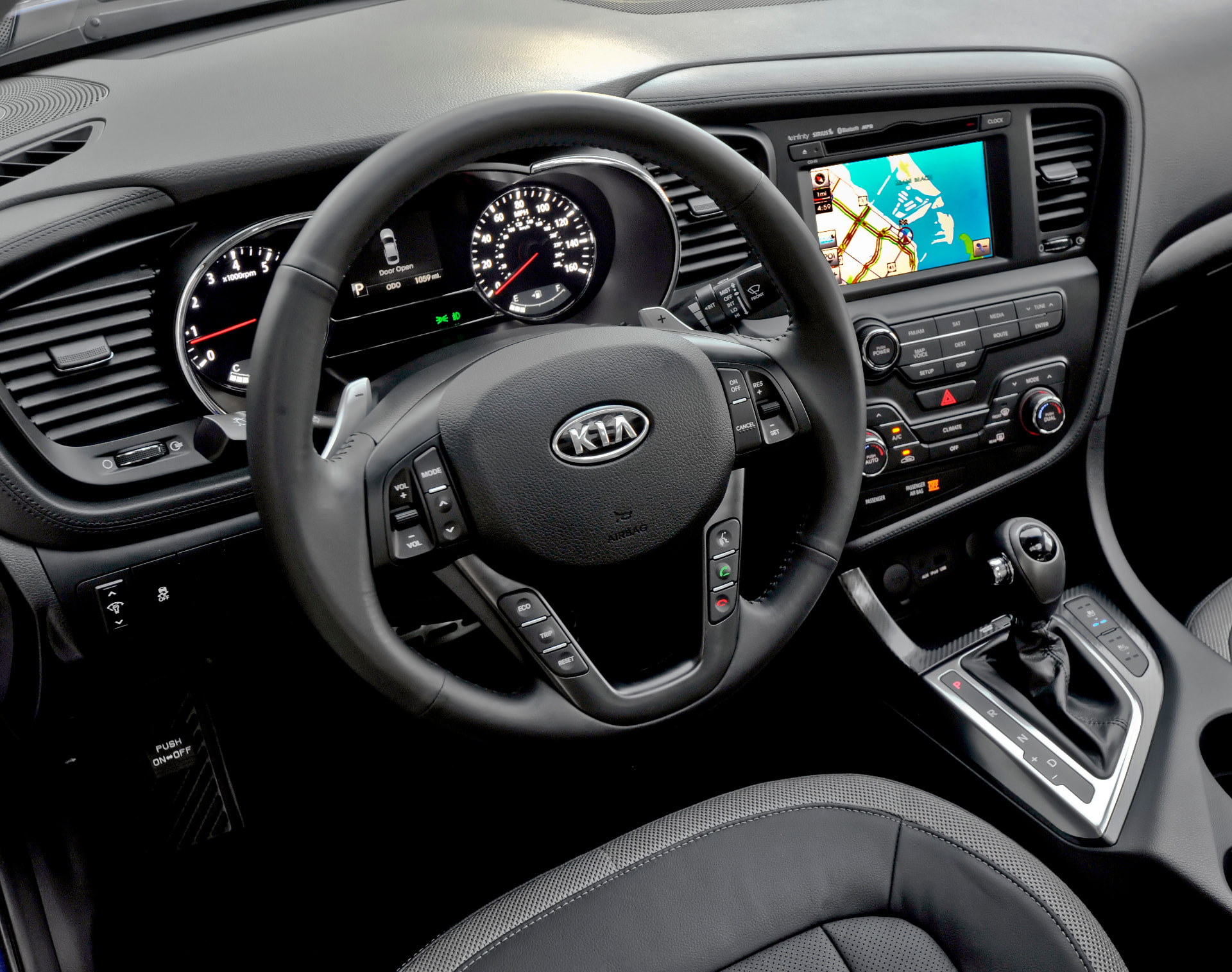 Kia Optima cockpit from the driver's seat showing the steering wheel, cluster, center stack, and shifter